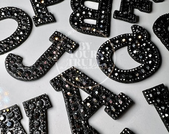 Peut inclure: Lettres de l'alphabet en strass noir. Les lettres sont en feutre noir et recouvertes de strass noirs.