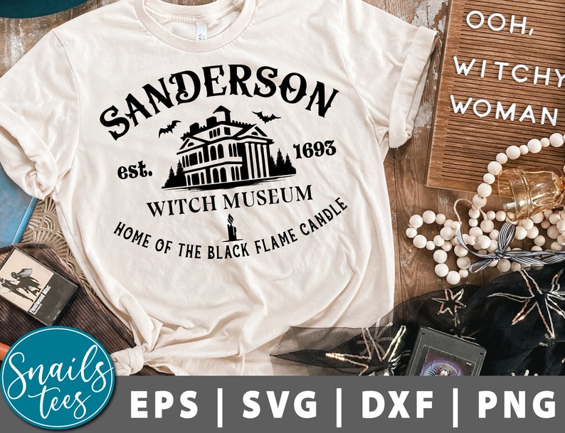 Pu&ograve; includere: Una maglietta bianca con un design grafico nero che presenta una casa con il testo "Sanderson est. 1693 Witch Museum Home of the Black Flame Candle".