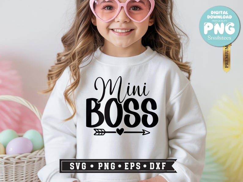 May include: White sweatshirt with the text "Mini BOSS" in black script and bold letters, with an arrow and heart design. The image includes a digital download badge and a basket with Easter eggs.