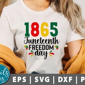 Puede incluir: Camiseta blanca con el texto "1865 Juneteenth Freedom Day" en letras verdes, rojas y amarillas. El texto está rodeado de pequeñas estrellas rojas, amarillas y verdes.