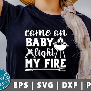Könnte beinhalten: Ein schwarzes T-Shirt mit weißem Text, der "come on baby light my fire" lautet. Der Text wird von einem Grill und Spießchen begleitet. Das Shirt wird von einer Person mit langen blonden Haaren getragen.