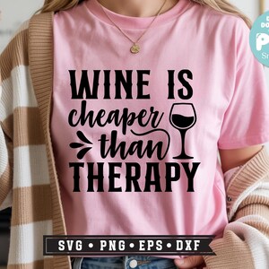 May include: Pink t-shirt with the phrase "WINE IS cheaper than THERAPY" in black lettering. A wine glass graphic is next to the text. The shirt also has SVG, PNG, EPS, and DXF file format options.