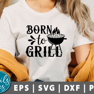 Może przedstawiać: Biała koszulka z czarnym napisem "Born to Grill" z grafiką grilla i płomieni.