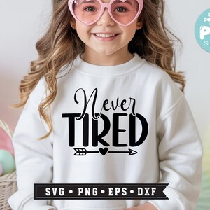 May include: A white sweatshirt with the words "Never Tired" in black script and block letters. Below the text is an arrow with a heart in the middle. The image also includes a digital download graphic.