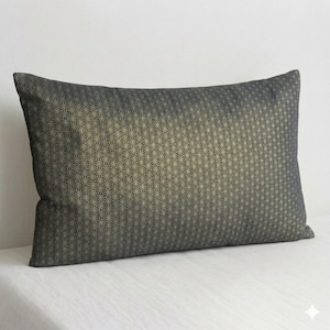 May include: Rectangular decorative pillow with a geometric pattern. The pillow features a repeating starburst design in shades of gray and gold. The pillow is placed on a white surface.