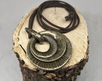 May include: A bronze pendant necklace with a layered circle design. The pendant is on a brown suede cord.
