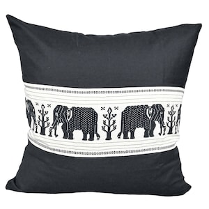 Puede incluir: Almohada negra y blanca con un borde decorativo que presenta un patrón repetido de elefantes y árboles. La almohada está hecha de una tela suave de color gris oscuro.