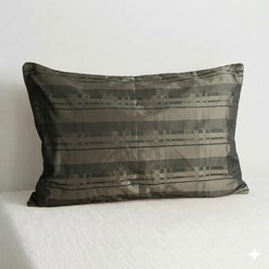 Può includere: Un cuscino decorativo rettangolare con un motivo a righe nei toni del verde oliva e del nero. Il cuscino ha un aspetto morbido e strutturato, adatto per un letto o un divano.