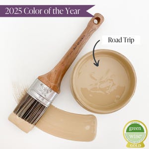 May include: A paint brush with a wooden handle and a beige paint sample. The paint color is called "Road Trip" and is the 2025 Color of the Year. The paint is certified by Green Wise Gold.