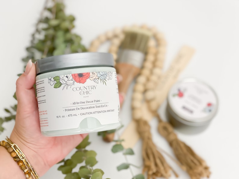 May include: A jar of Country Chic paint in a light green color with a floral design on the label. The label reads "All-In-One Decor Paint" and "Peinture De Decoration Tout En Un". The jar is 16 fl oz or 475 ml.