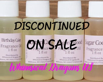 May include: Four small fragrance oil bottles with white caps. The bottles have labels with the text "Birthday Cake", "Cotton Candy", "Dragon Blood", and "Sugar Cookie". The words "DISCONTINUED" and "ON SALE" are written across the bottles.
