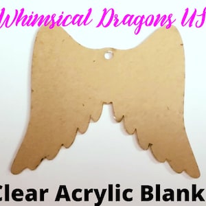 May include: A pair of brown, unfinished, wooden angel wings with a hole at the top for hanging. The wings have a scalloped edge and are shaped like a traditional angel wing. The wings are labeled "Whimsical Dragons US" and "Clear Acrylic Blanks".