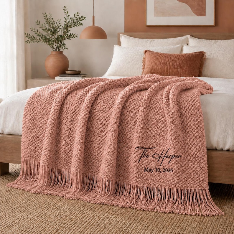 May include: A dusty rose textured knit throw blanket featuring long fringe trim along the bottom edge. The blanket is embroidered with the black script text "The Harper" followed by the date "May 10, 2026" in a simple sans-serif font.