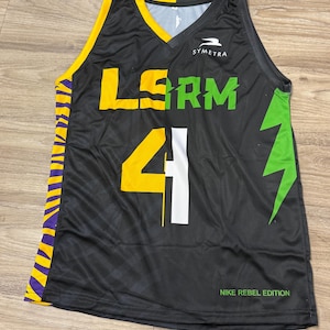 May include: Black basketball jersey with yellow and green accents. The jersey features the word "LSRM" in yellow and green, the number "41" in yellow and white, and the text "NIKE REBEL EDITION". The jersey has a V-neck and the brand name "SYMETRA".