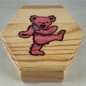 May include: Wooden hexagonal box with a dancing bear design on the lid. The bear is depicted in shades of pink and red on one box and orange on the other. The box is made of light-colored wood.
