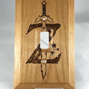 May include: A wooden light switch cover with a wood-burned design of a sword and a stylised letter Z.