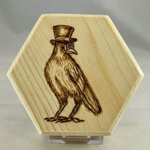May include: A wooden hexagonal plaque with a woodburned image of a crow wearing a top hat and goggles.