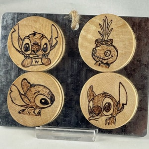 Puede incluir: Cuatro posavasos de madera con fondo negro. Cada posavasos presenta un personaje de dibujos animados diferente, incluyendo Stitch de Lilo & Stitch y un personaje de Pesadilla antes de Navidad.