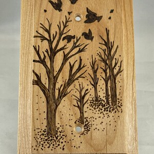 May include: A wooden light switch cover with a woodburned design of trees and birds. The design is in shades of brown and black.
