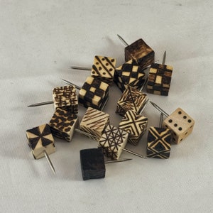 Puede incluir: Una colección de 14 chinchetas de madera con patrones geométricos en blanco y negro. Las chinchetas están dispuestas en un grupo sobre una superficie blanca.