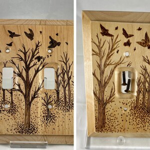 May include: A wooden light switch cover with a woodburned design of trees and birds. The switch cover has two toggle switches.