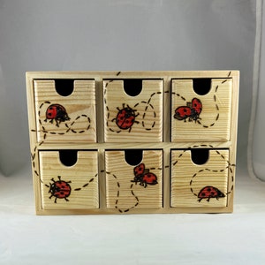 May include: A wooden drawer organizer with six small drawers, each decorated with a red ladybug design and a black dotted line.