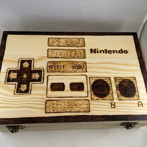 May include: A wooden box with a burnt-in design of a Nintendo controller. The box has a dark brown border and the words "Nintendo", "Select", "Start", "A", and "B" are burnt into the wood.