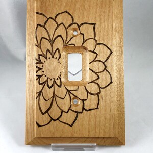 May include: A light brown wooden light switch cover with a laser-etched mandala design.