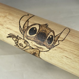 Puede incluir: Un rodillo de madera con una imagen quemada de Stitch de Lilo & Stitch sosteniendo un pequeño juguete de peluche. El rodillo es de color marrón claro con una superficie lisa.