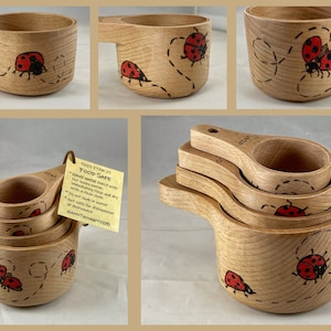 May include: Set of four wooden measuring cups with ladybug designs. The cups are nested together and have a brown wood finish. The ladybugs are painted in red and black with white spots. The cups are hand-painted and food safe.