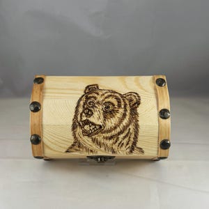 May include: A wooden box with a bear face carved into the lid. The box has metal accents and a hinged lid.