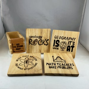 May include: Set of five wooden coasters with funny science and math themed sayings. The coasters feature sayings like "Geology Rocks", "Geography is Where It's At", "Never Trust an Atom They Make Up Everything", and "Math Teachers Have Problems".