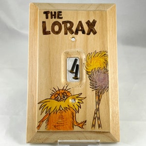 May include: A wooden light switch cover with a hand-painted image of the Lorax from the Dr. Seuss book. The cover features the text "THE LORAX" in brown lettering.