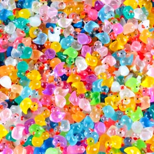 Puede incluir: Imagen de primer plano de una colección de pequeñas cuentas con forma de pato, de colores brillantes. Las cuentas son de tonos amarillos, naranjas, rosas, azules, verdes y blancos. La imagen muestra los detalles de las formas de pato.