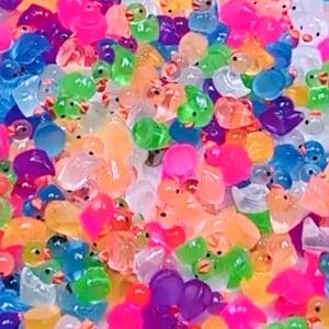 Puede incluir: Un vibrante surtido de juguetes con forma de pato translúcidos y coloridos. Los patos son de varios tonos de rosa, verde, azul, naranja y morado. Los juguetes son pequeños y parecen estar hechos de un material gelatinoso.
