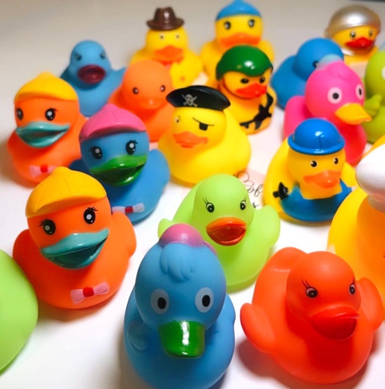 May include: A collection of colorful rubber ducks in various designs, including a pirate with an eye patch, a duck with a brown hat, a construction worker with a blue hard hat, and others in shades of orange, blue, yellow, pink, and green.