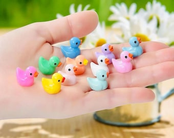 May include: A collection of twelve miniature plastic ducks in various pastel and bright colors including pink, yellow, green, blue, orange, white, and purple. Each small duck figurine features a smooth finish, a tiny orange beak, and black eyes.