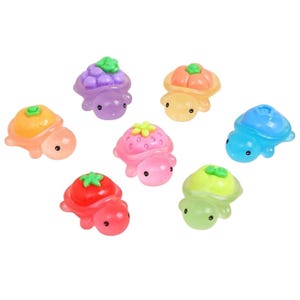 Puede incluir: Una colección de figuras de tortugas translúcidas de colores, cada una coronada con un diseño de fruta diferente. Las tortugas son en tonos de rosa, naranja, verde, azul y morado, con diseños de fresa, uva y tomate.
