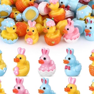 May include: A selection of colourful Easter-themed figurines. The collection includes yellow ducklings in baskets and wearing bonnets, and ducklings with bunny ears in pink and blue. The figurines are small and brightly coloured.