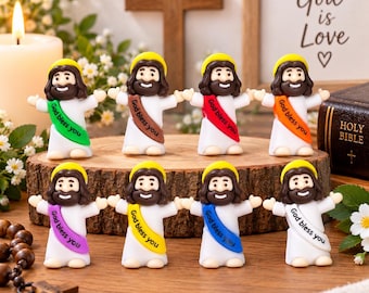 May include: Eight small figurines of a smiling figure with long brown hair and a beard, wearing a white robe with a colored sash printed with the text God bless you. The sashes are green, brown, red, orange, purple, yellow, blue, and white.
