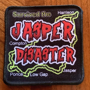 May include: Black embroidered patch with the text "Survived the Jasper Disaster" in red and yellow. The text is surrounded by a green outline of a map with place names like "Harrison", "Compton", "Ponca", "Low Gap", and "Jasper".