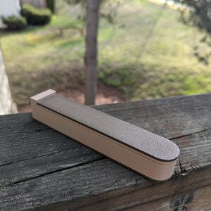 May include: A brown and beige rectangular box with a rounded edge. The box is made of a textured material and has a smooth, flat top.