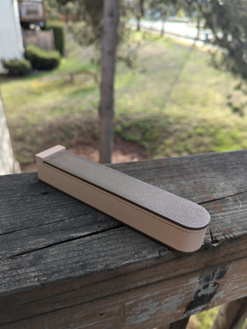 May include: A brown and beige rectangular box with a rounded edge. The box is made of a textured material and has a smooth, flat top.