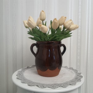 Puede incluir: Un ramo de tulipanes artificiales de color crema en un jarrón de cerámica marrón con base redonda. El jarrón tiene un esmalte marrón y un borde de color terracota.