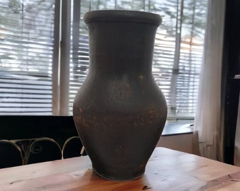 May include: A dark gray ceramic vase with a rounded body and a wide opening. The vase is sitting on a wooden surface.