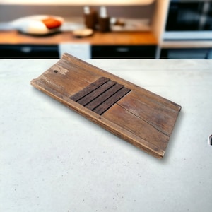 Puede incluir: Un rallador de verduras vintage de madera con cinco cuchillas de metal. El rallador es de madera marrón claro y tiene una forma rectangular.