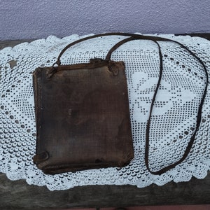 May include: A brown leather satchel bag with a long strap. The bag is sitting on a white crocheted doily.