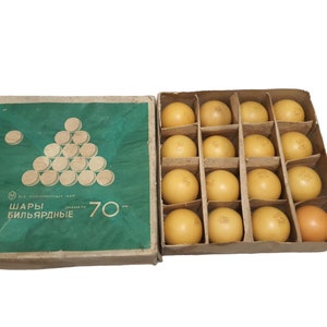 Op de afbeelding: Een set van 16 biljartballen in een bruine kartonnen doos. De ballen zijn lichtbruin van kleur en hebben bedrukte nummers. De doos heeft een groene achtergrond met de tekst "ШАРЫ БИЛЬЯРДНЫЕ" en "70 мм" erop gedrukt.