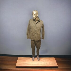 May include: A brown workwear jacket and matching trousers on a mannequin. The jacket has a button-up front and two pockets. The trousers have a straight leg.
