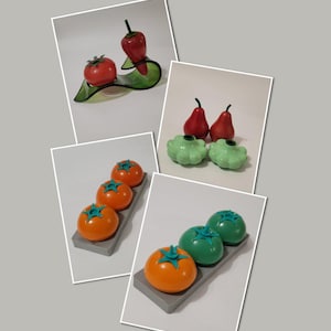 May include: A set of three ceramic tomato salt and pepper shakers. The shakers are orange and green with a green star on top. The shakers are on a gray tray.